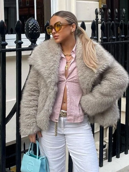 Woman wearing a gray fur coat, pink shirt, and white pants standing in front of a black iron gate.